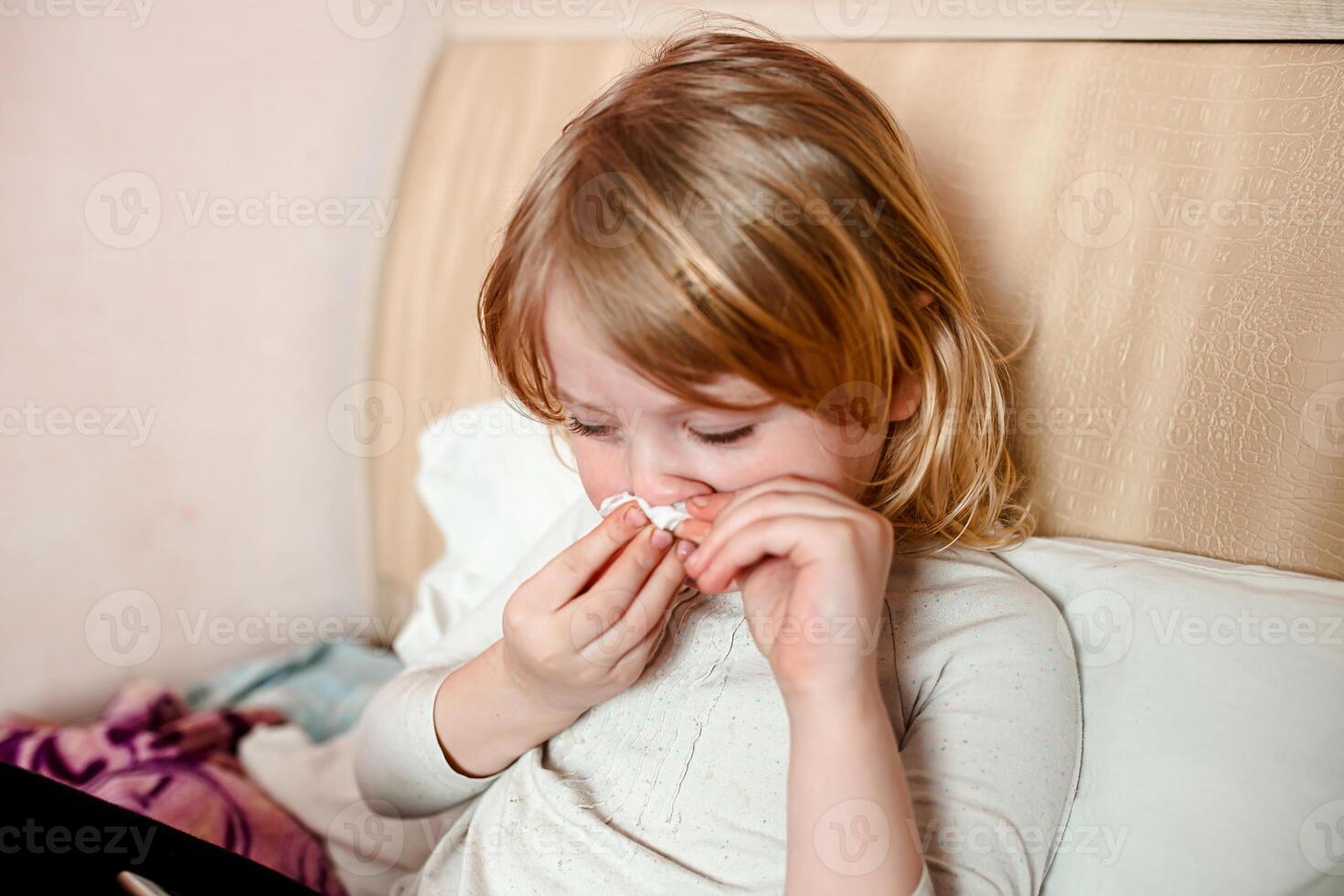 Sick little girl with flu lying in bed and blowing her nose photo