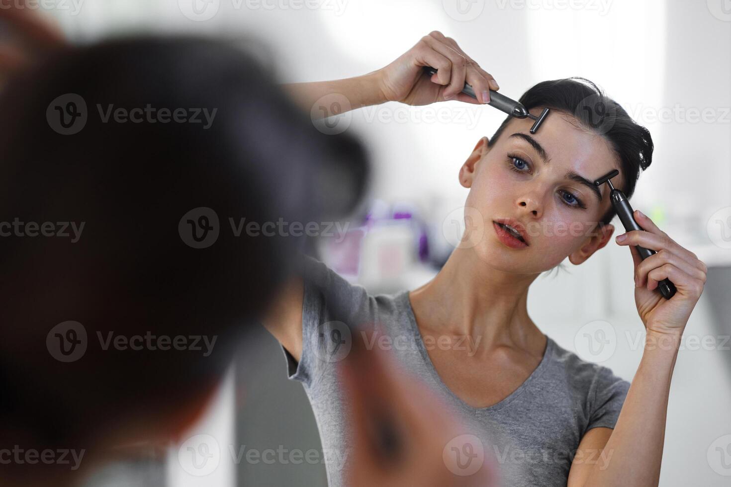 A young woman massages her face with gouache while looking in the mirror. photo