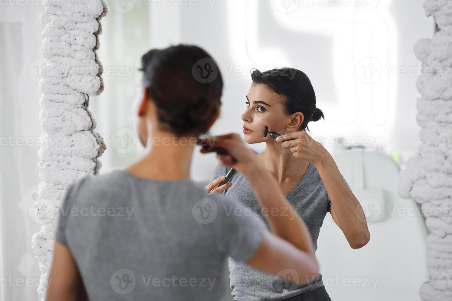 A young woman massages her face with gouache while looking in the mirror. photo