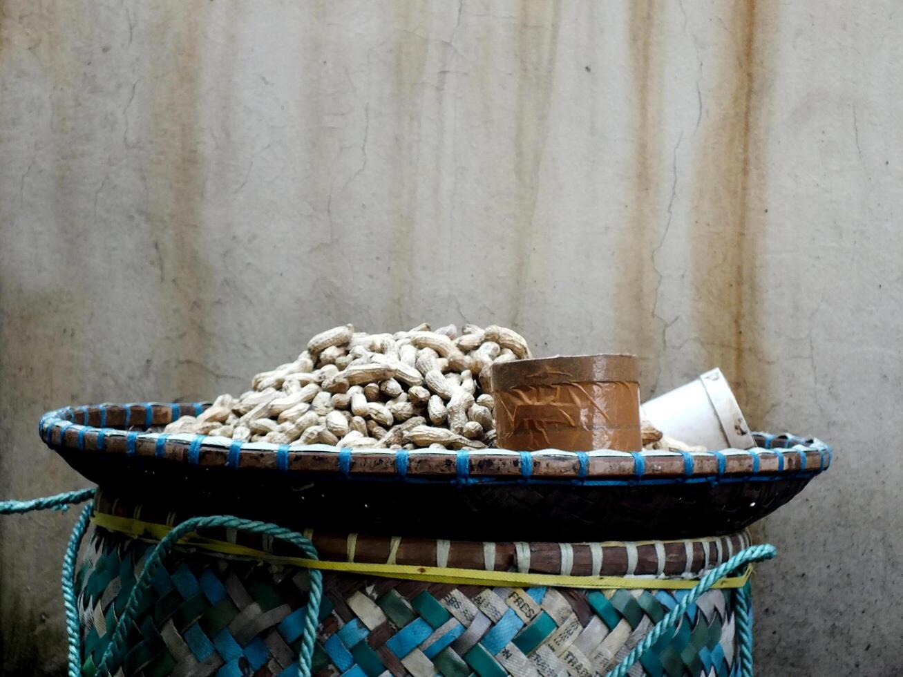 close up of a peanut seller's bamboo basket. the basket is green, there is a cans, and a pile of boiled beans ready to be sell photo