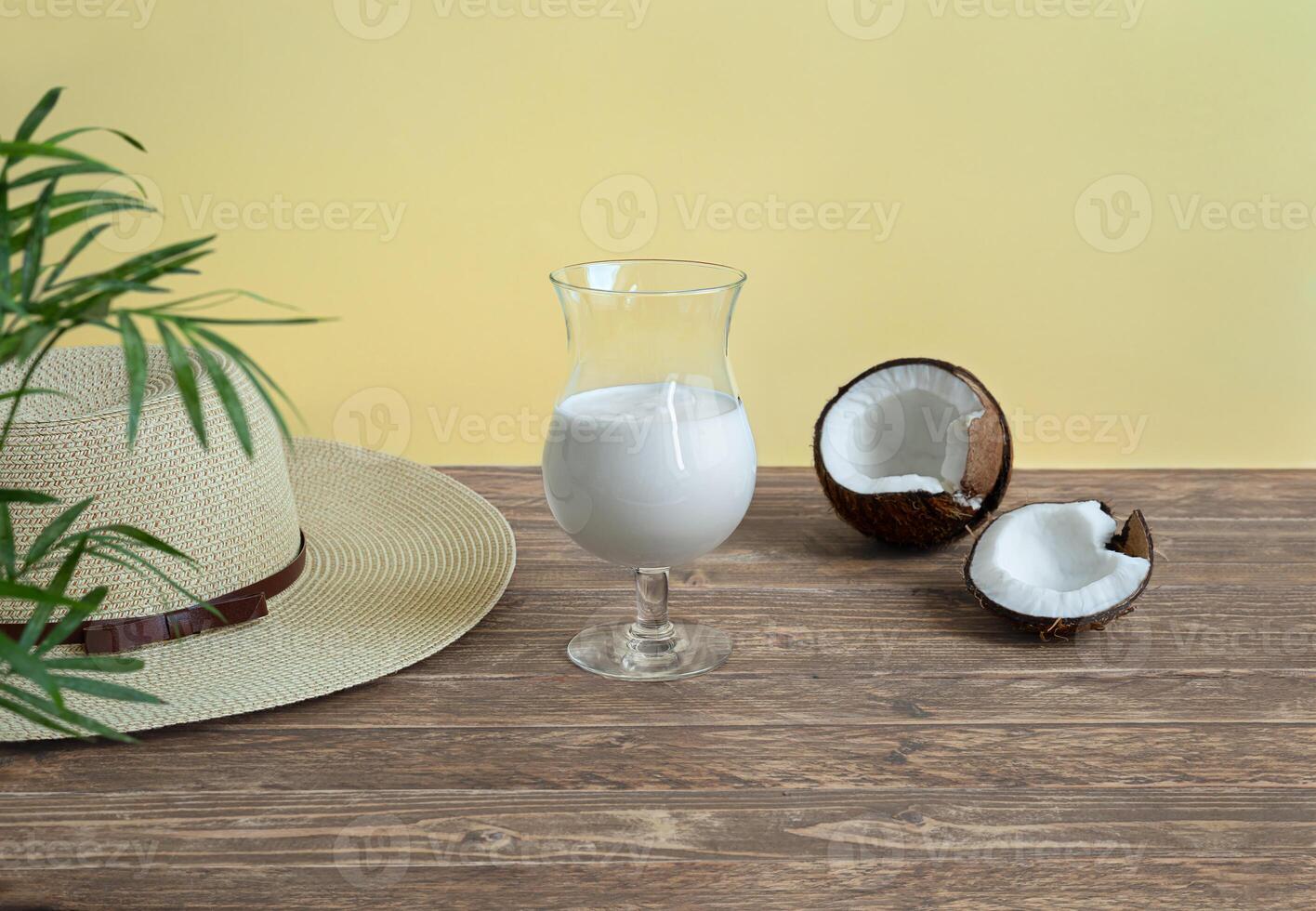 A glass of coconut milk cocktail and a summer hat on wooden table photo
