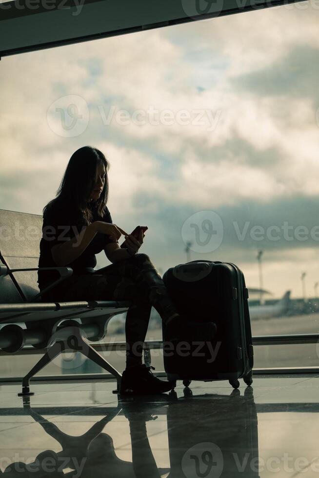 A woman with her suitcase checks her mobile phone at the airport while the cloudy sky is seen in the background. photo