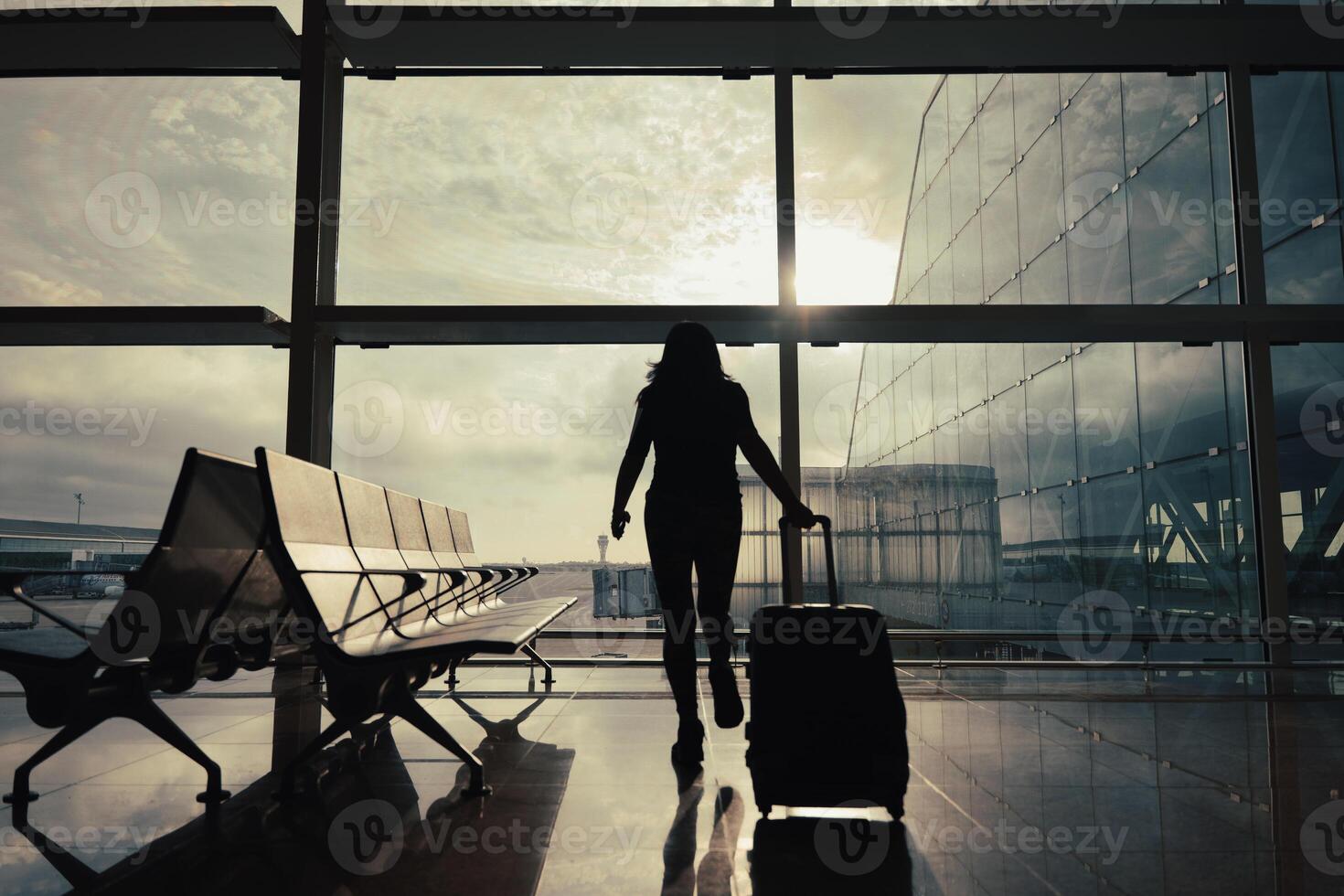 Woman with suitcase walks through the airport departure hall while the sun's rays come through the window. photo