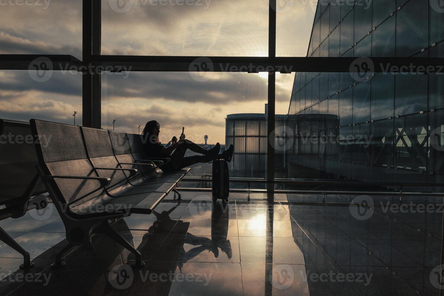 Woman waits for her flight at the airport while the sun rises through the clouds in the sky. photo