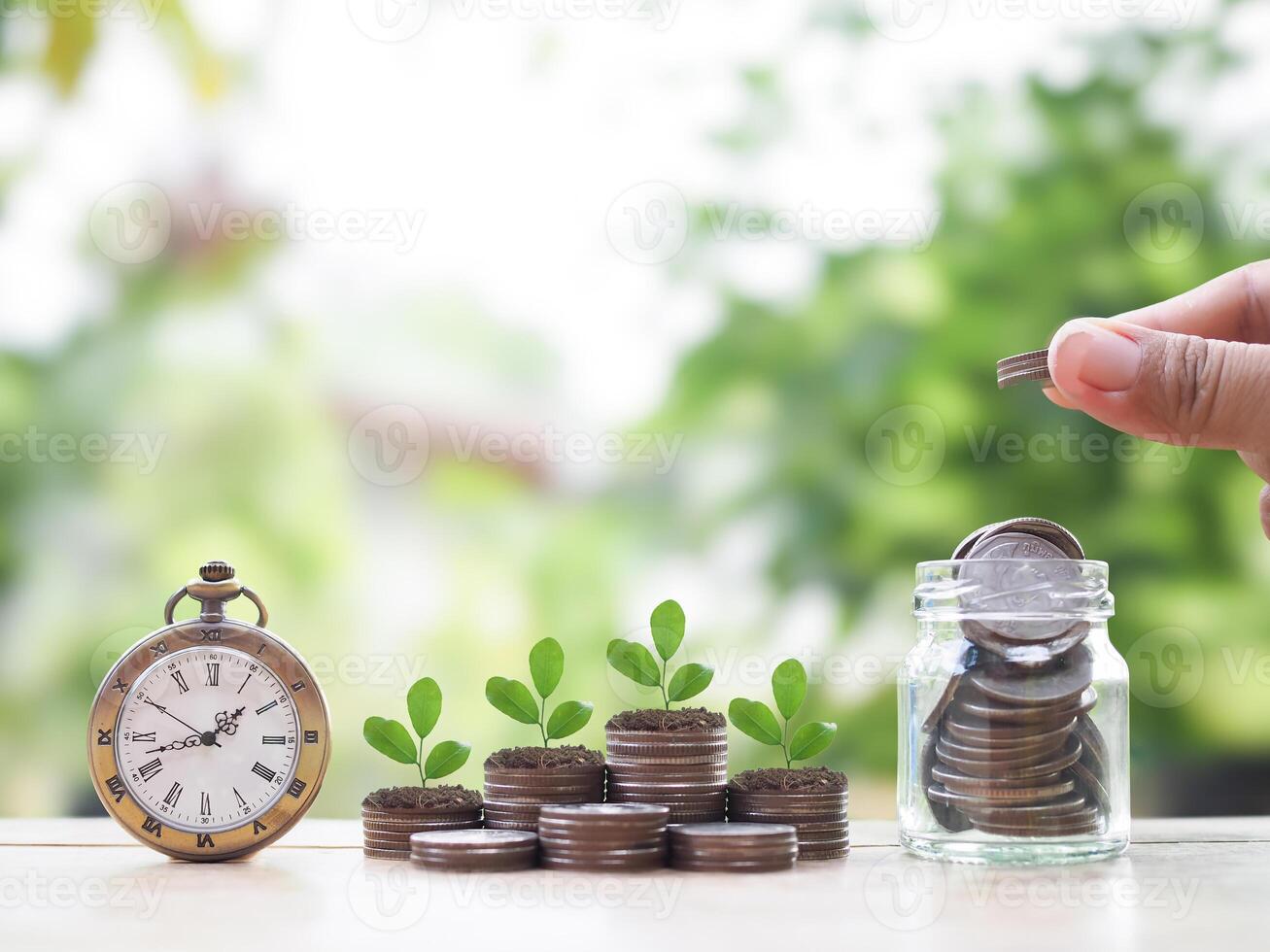 Close up hand putting coin into glass bottle, Vintage watch and Plants growing up on stack of coins. The concept of saving money, Financial, Investment and Business growing up. photo