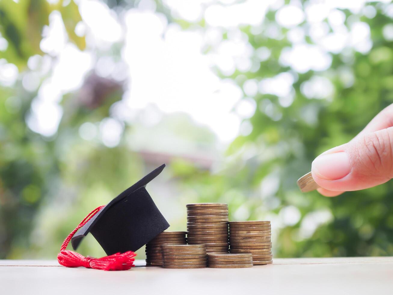 Close up of hand putting coins in stack of coins with graduation hat. The concept of saving money for education, student loan, scholarship, tuition fees photo