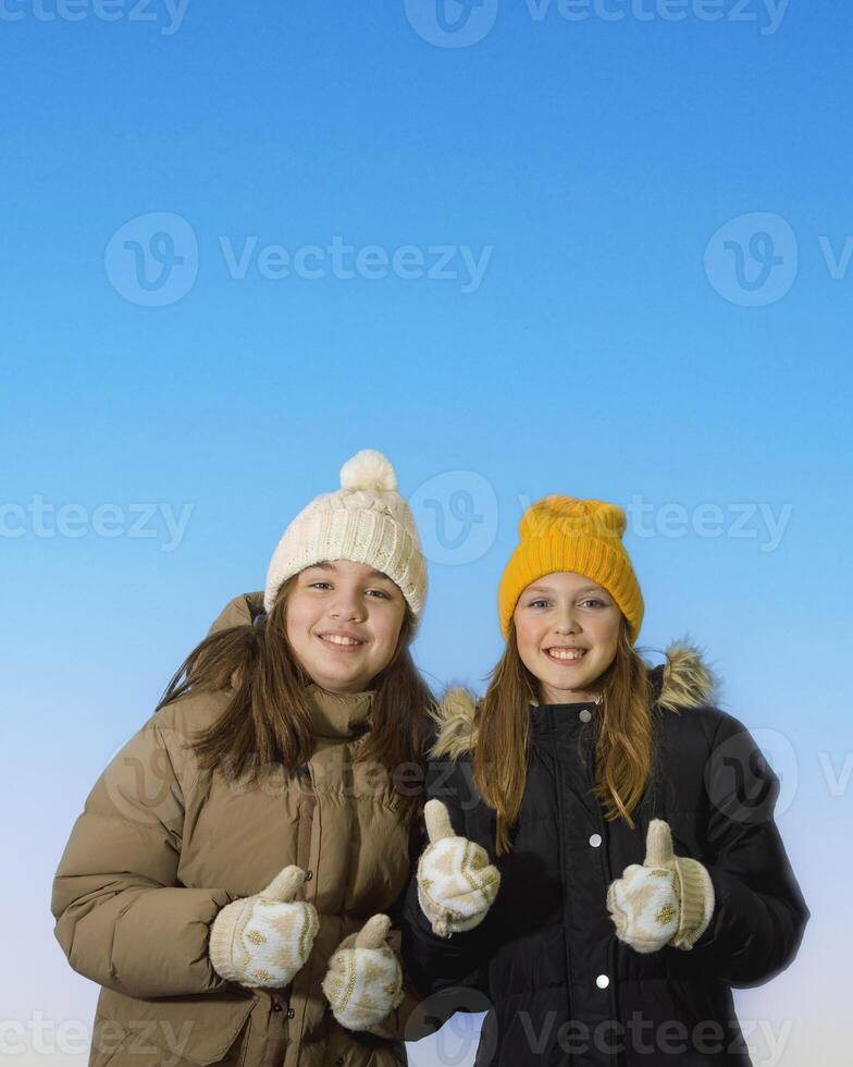 Two girlfriends portrait in winter clothes. Winter motif and clothes. studio photo. Sweaters, scarves, gloves. Joy on the faces. On blue background photo