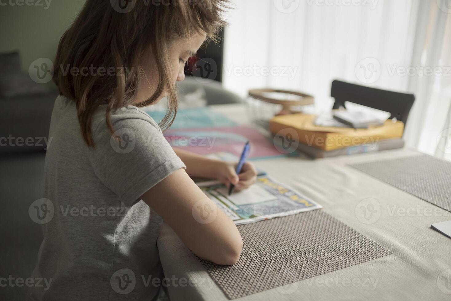 Teenage girl at home at the table solves a crossword puzzle photo