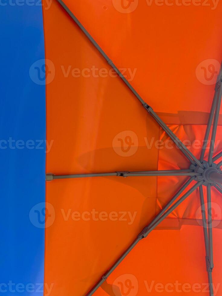 Low angle view of orange beach or poolside umbrella against a blue sky, holiday or vacation concept photo