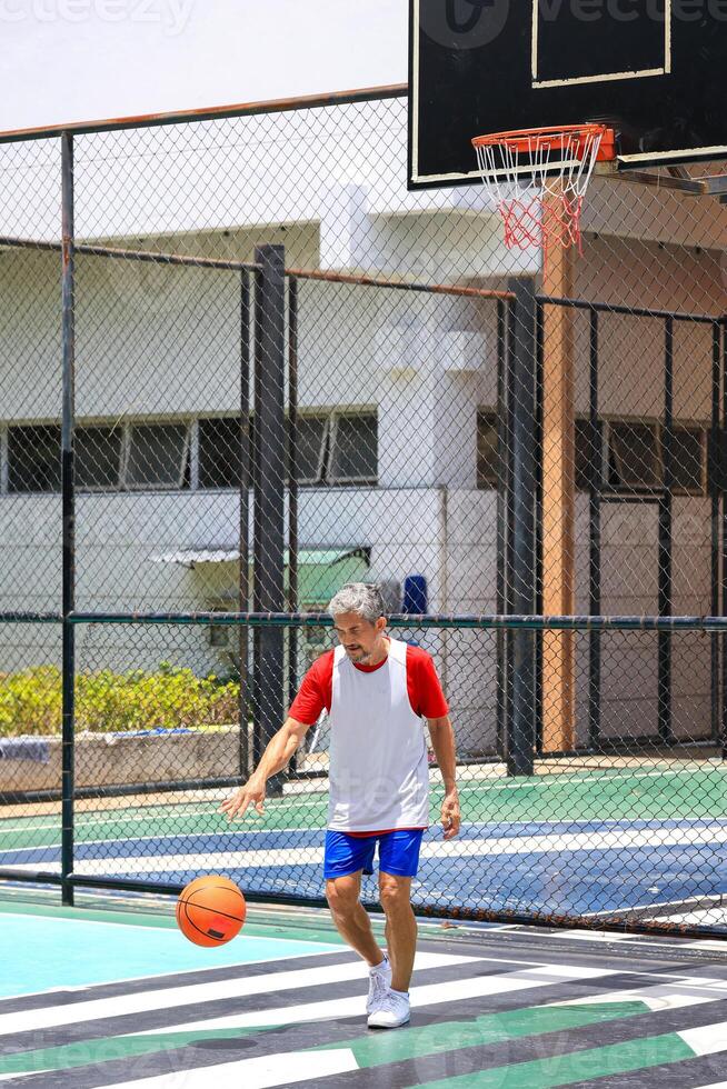 Senior Asian man in retirement age is playing basketball at outdoor court for healthy and fun activity to exercise and workout against aging illness photo