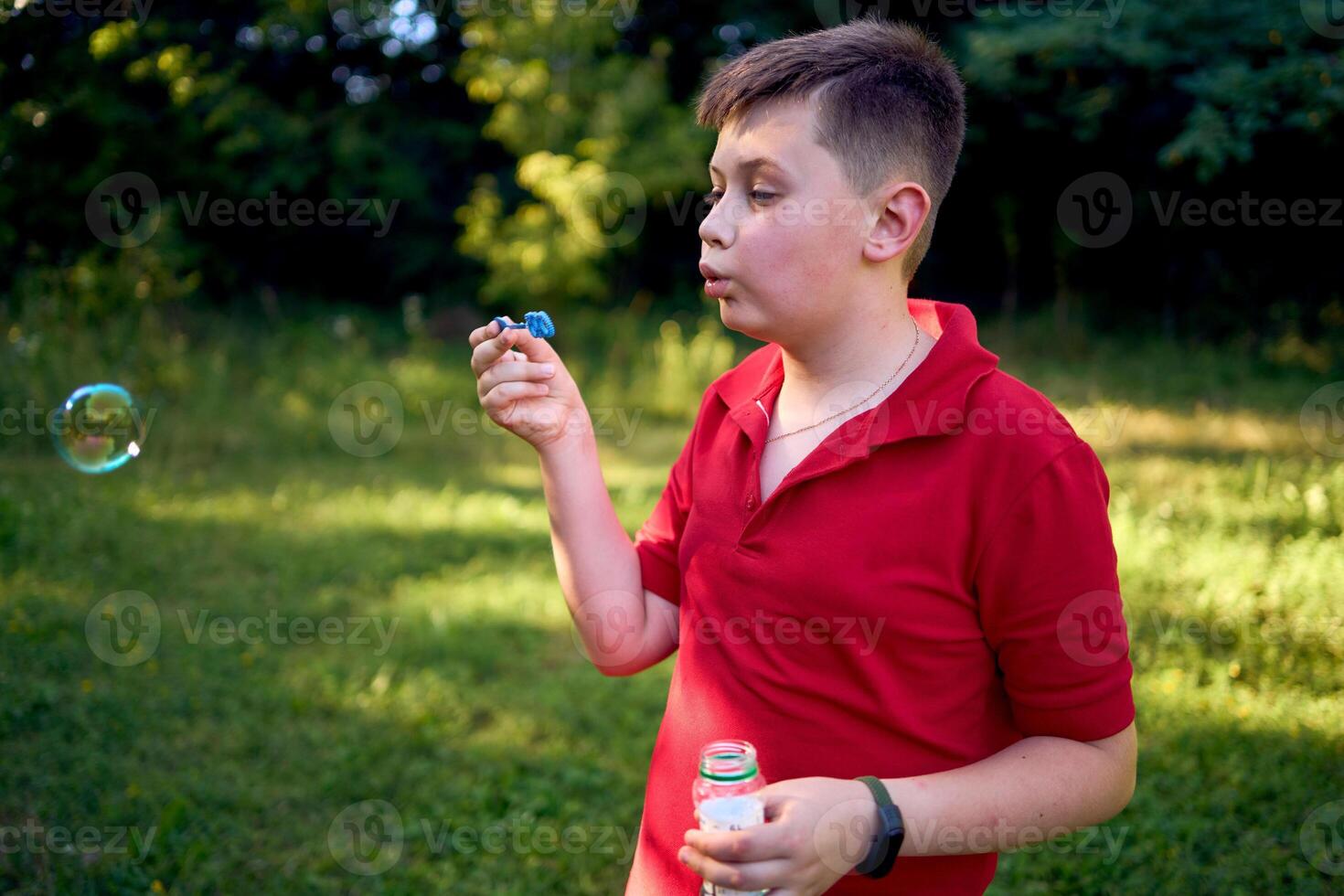 a preteen boy in a red T-shirt catches soap bubbles in the park photo