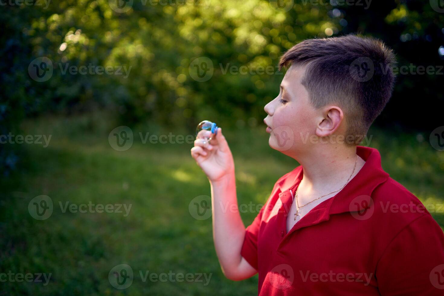 a preteen boy in a red T-shirt catches soap bubbles in the park photo