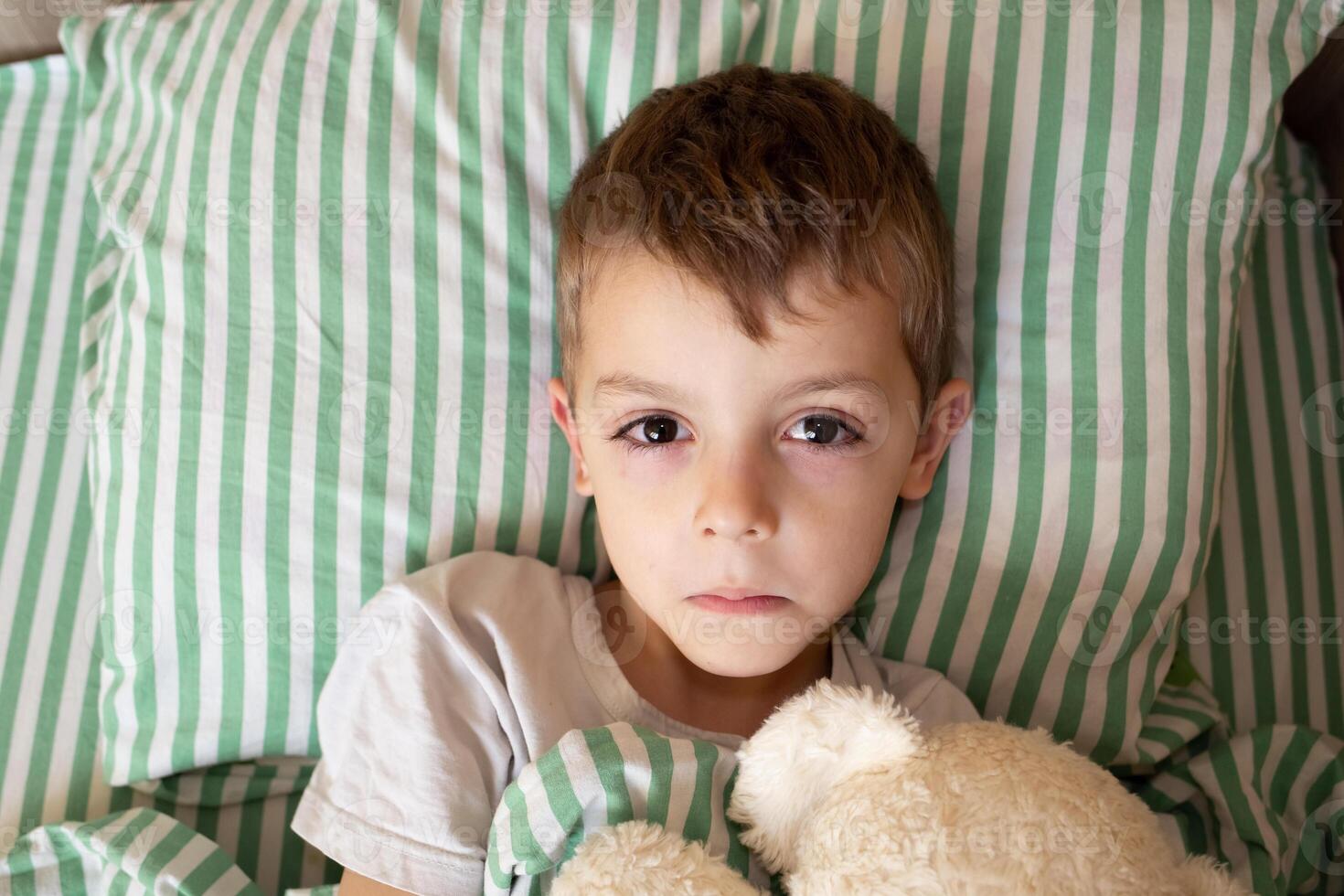 Unhealthy little boy child sleep in bed relax at home in bedroom. Sick ill little kid suffer from flu fever asleep in bed on lockdown quarantine photo