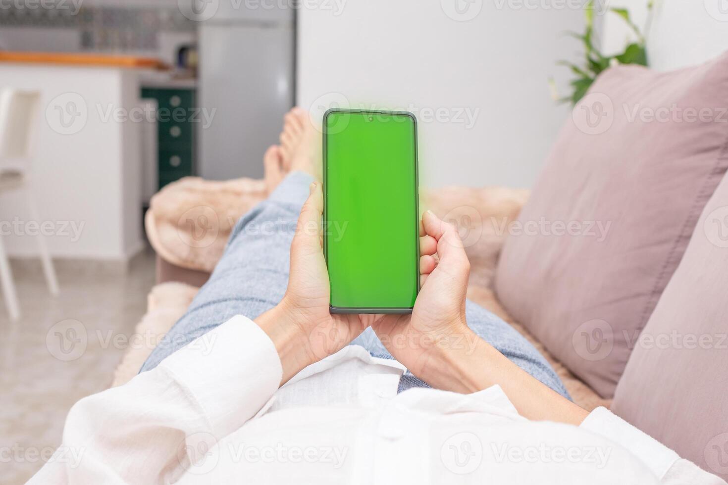 a man looks at a green chroma key screen on his phone while lying on the sofa in his living room.blurred background. photo