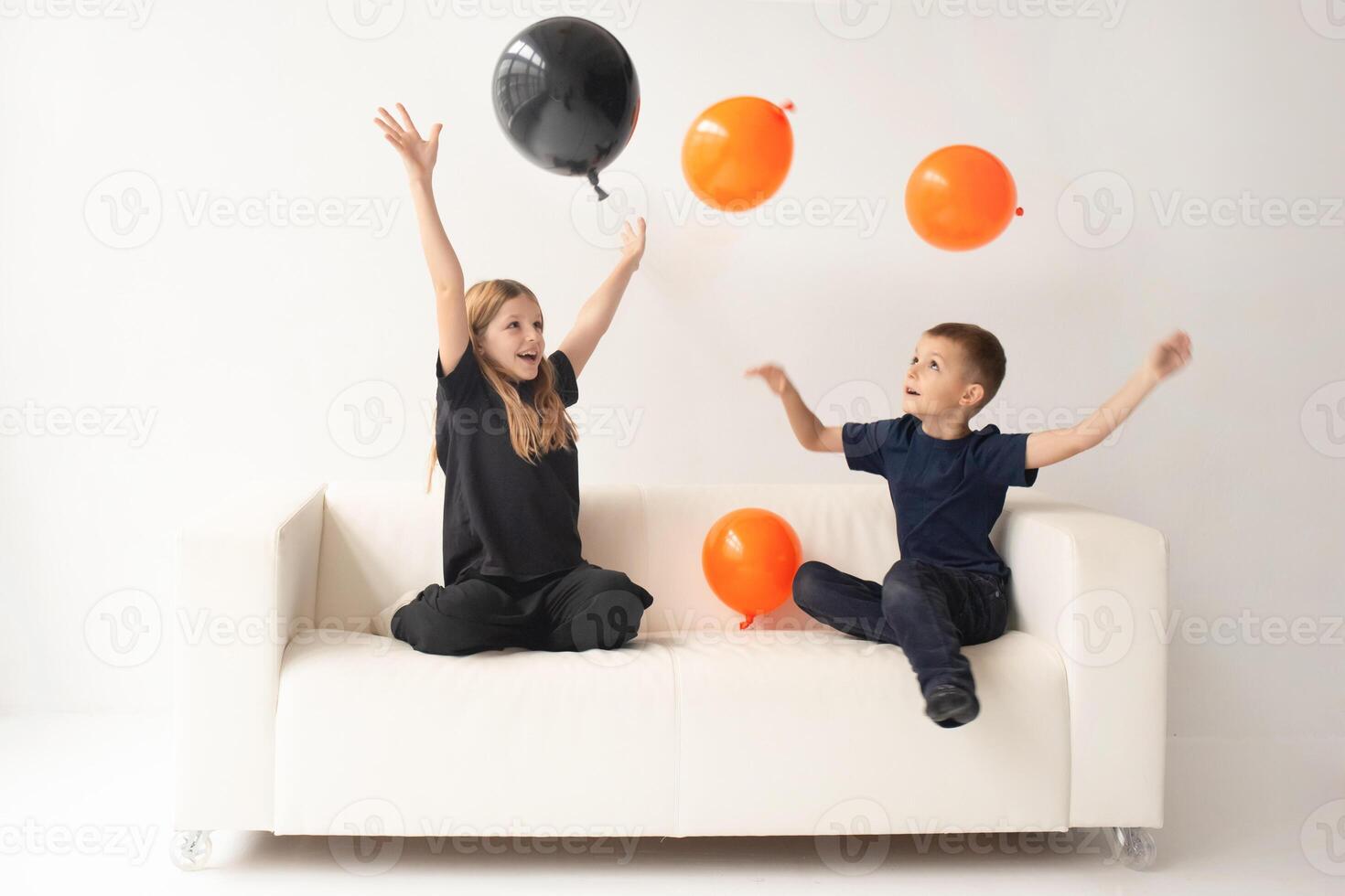 a boy and a girl in a large bright room play with black and yellow balloons in the colors of Halloween. White background photo