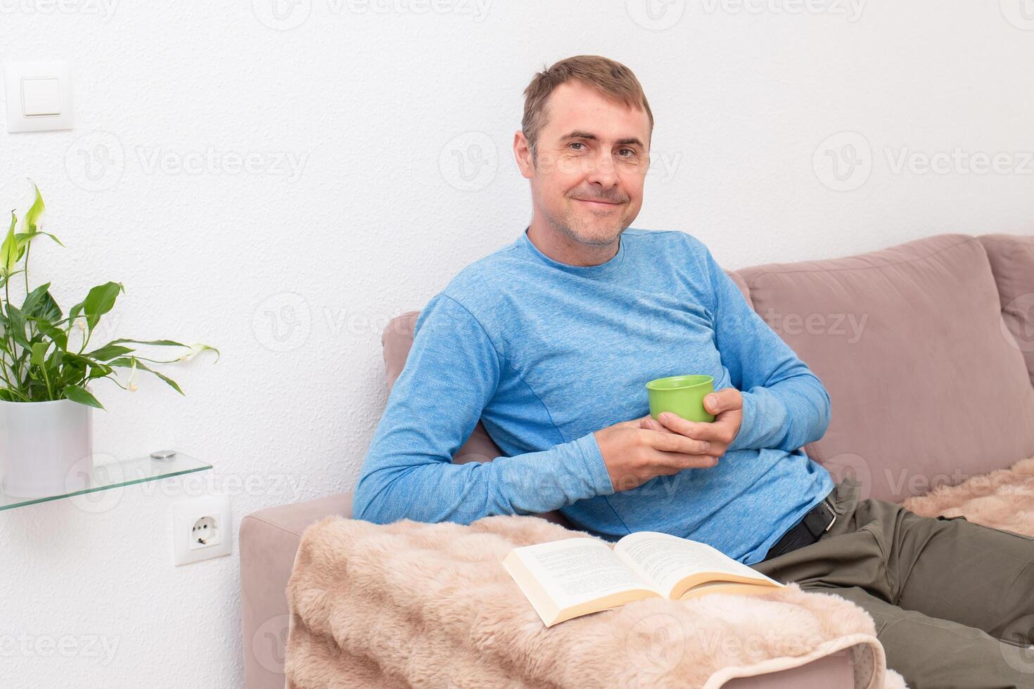 Relaxing at home, a man sits on the sofa and reads a book in front of him, enjoying a quiet moment photo