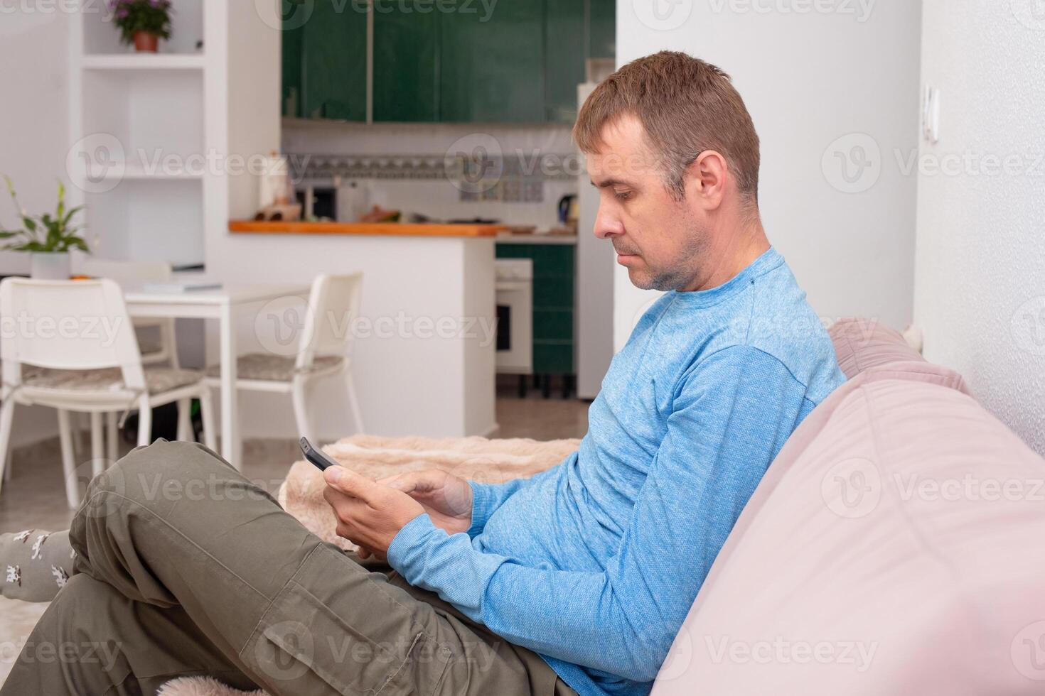 A cheerful man is texting his friends and agreeing on a meeting place while sitting on the sofa in his living room photo