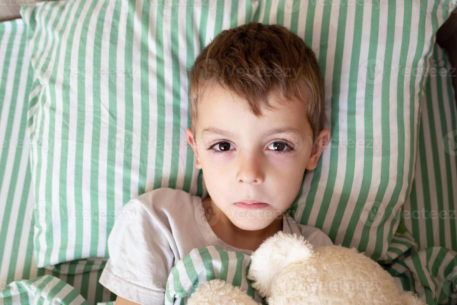 Unhealthy little boy child sleep in bed relax at home in bedroom. Sick ill little kid suffer from flu fever asleep in bed on lockdown quarantine. portrait of a sick child photo