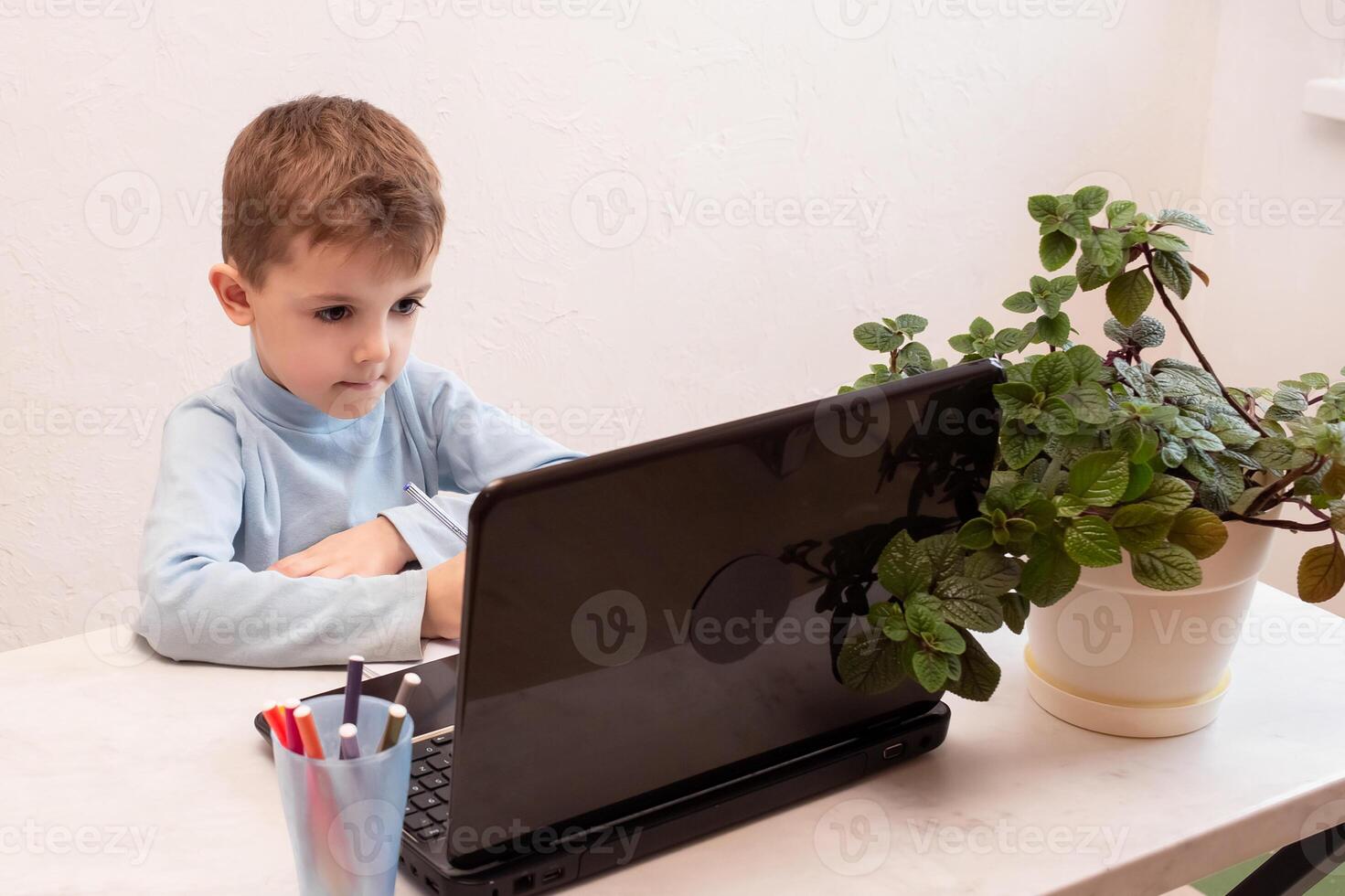 child student returns to school. boy smiles, writes or draws and reads on laptop while doing homework. teaching people at home in bedroom, studying online on computer photo