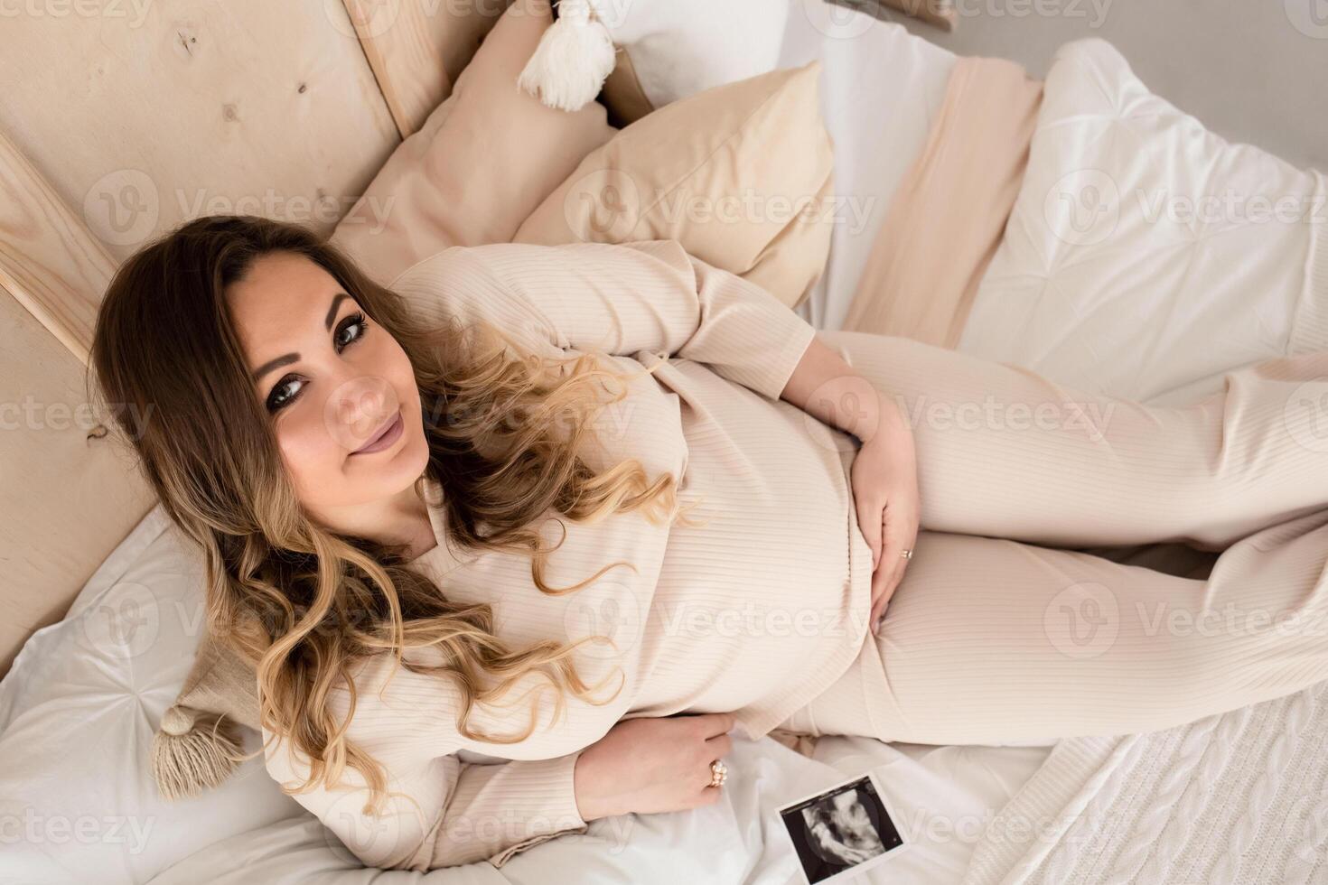 close-up of a pregnant woman on the bed hugging her pregnant belly. a beautiful pregnant woman lies on a sofa in a large beautiful living room near the window photo