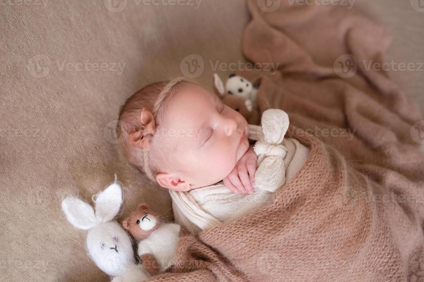 close-up portrait. a beautiful baby sleeps with knitted toys on a beige background covered with a soft, fluffy blanket. photo