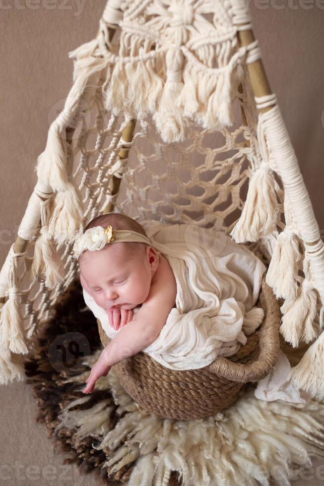 a beautiful baby sleeps in a wicker basket that stands in a wicker tent. beige background with space for text with baby sleeping in a wicker basket photo