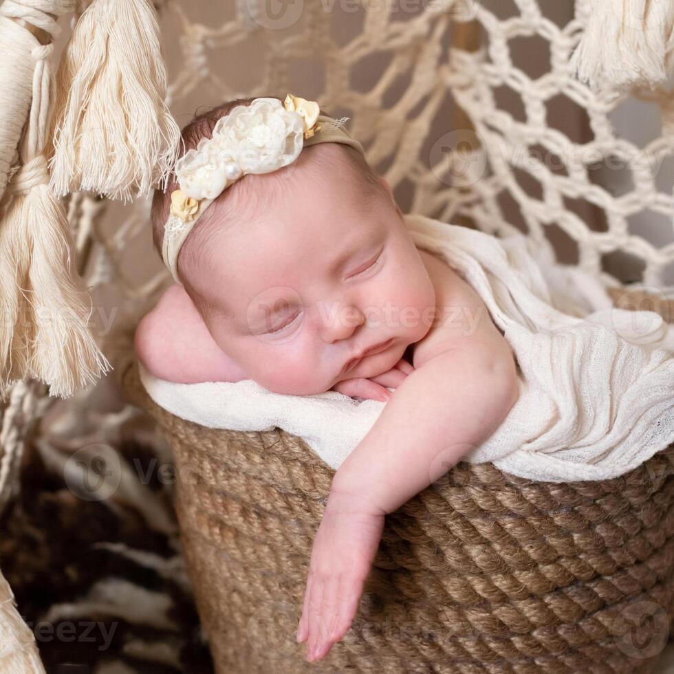 beige background with space for text with baby sleeping in a wicker basket decorated with blue orchid flowers. beautiful sleeping baby on a beige background. a beautiful baby sleeps in a wicker basket photo