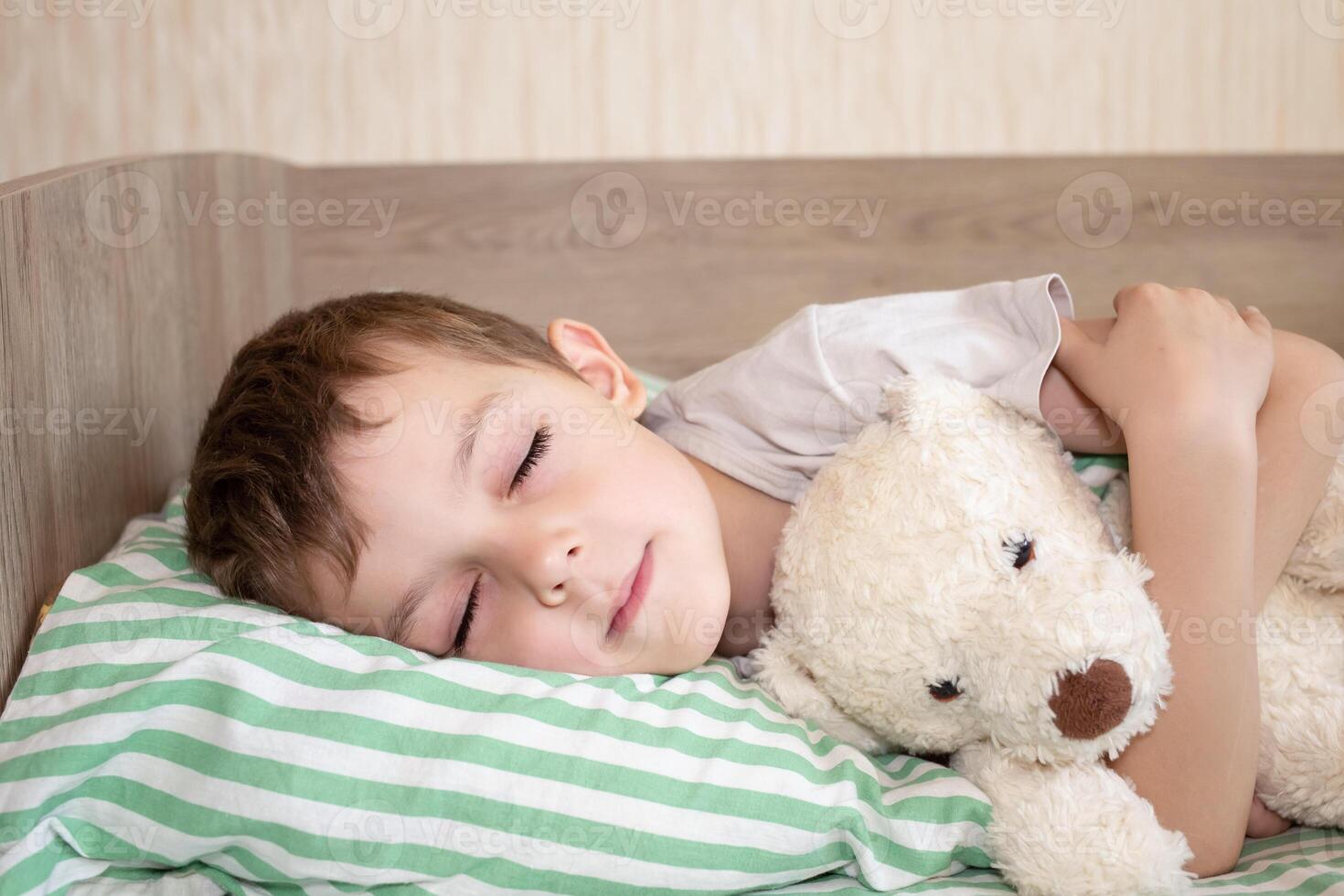 adorable boy sleeping in bed with bear toy. six year old baby sleeping at home photo