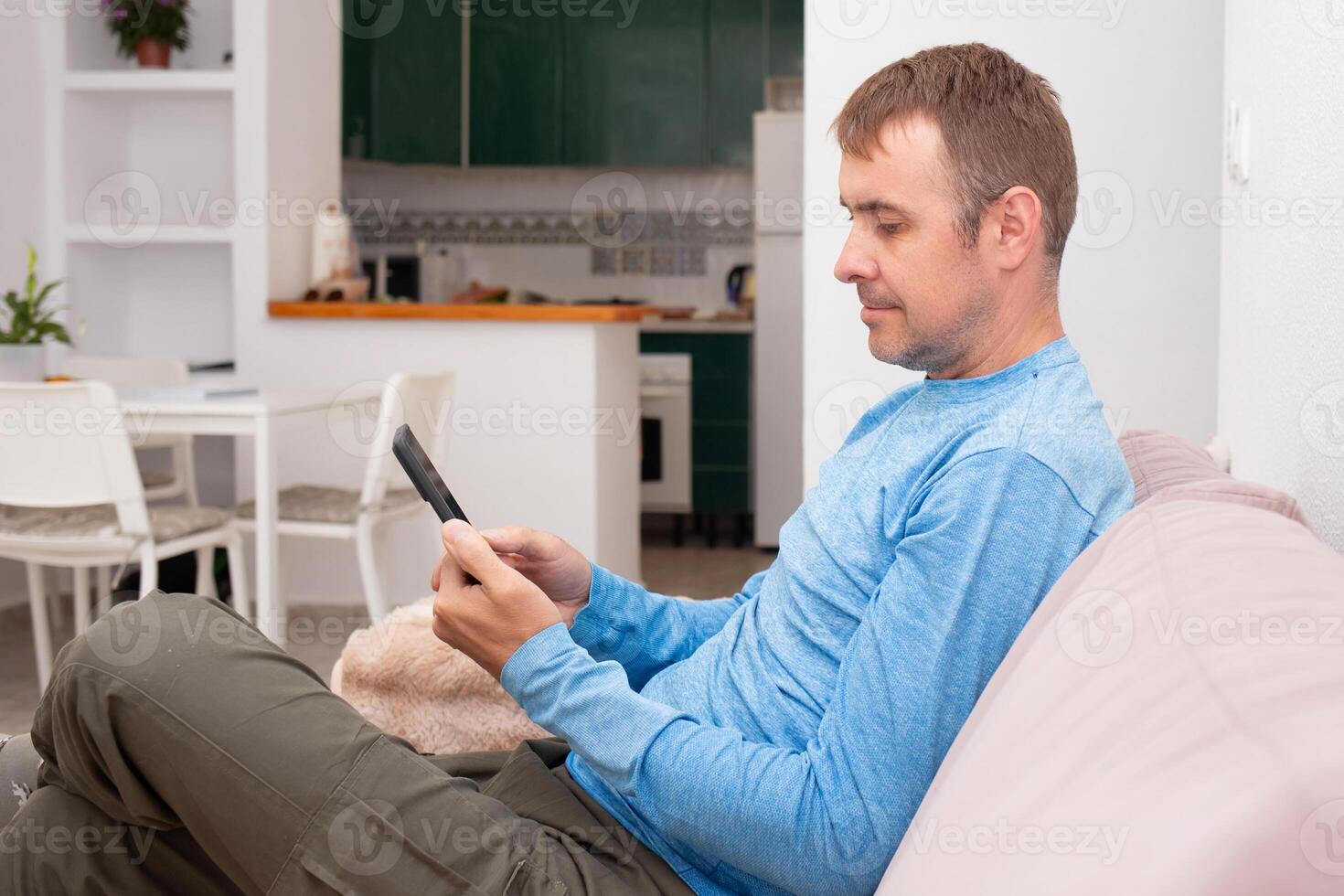 A cheerful man is texting his friends and agreeing on a meeting place while sitting on the sofa in his living room photo