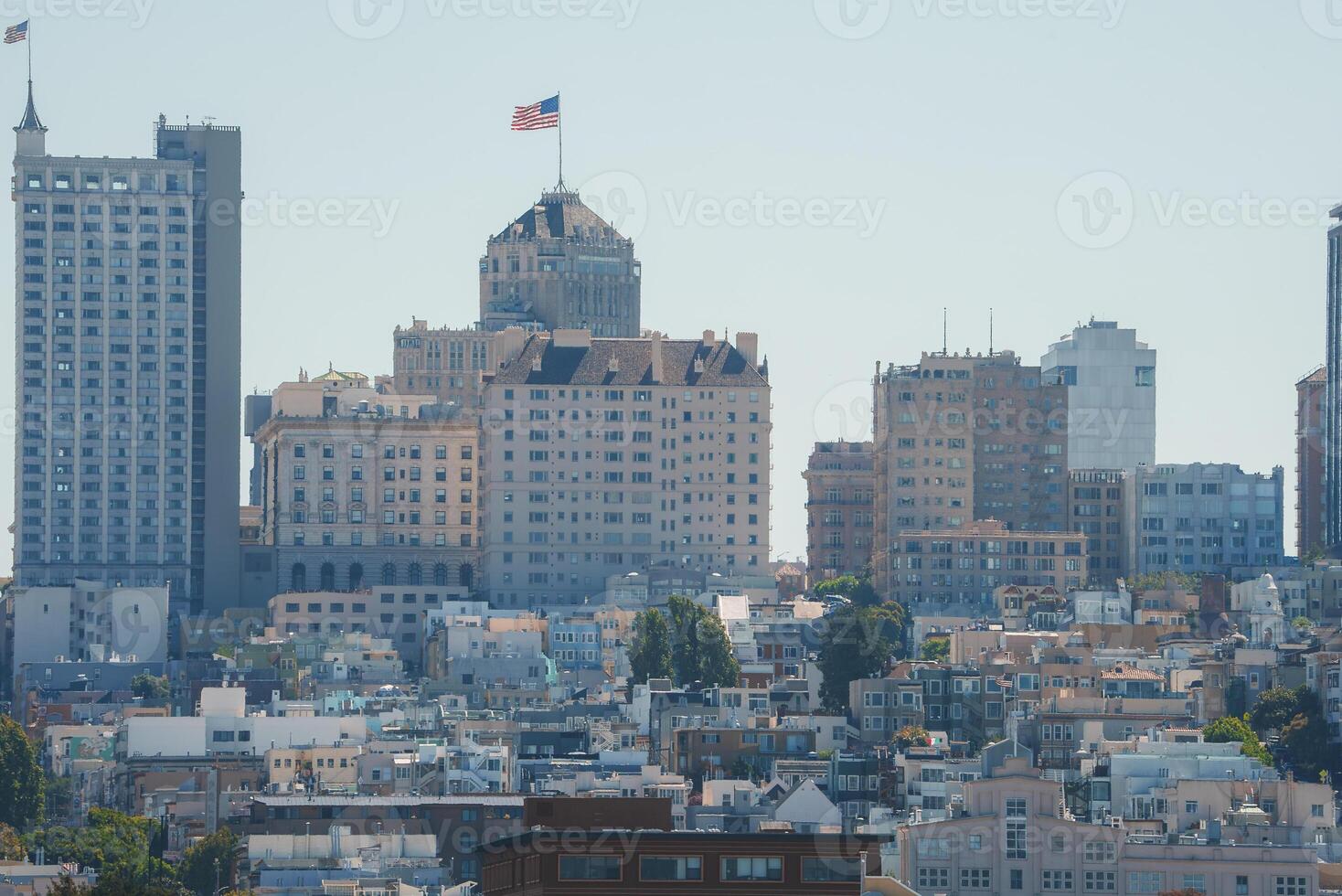 Daytime view of San Francisco's urban landscape. Iconic hilly terrain with buildings of varying heights. Dominant building with peaked roof and flag. Storied city architecture. photo
