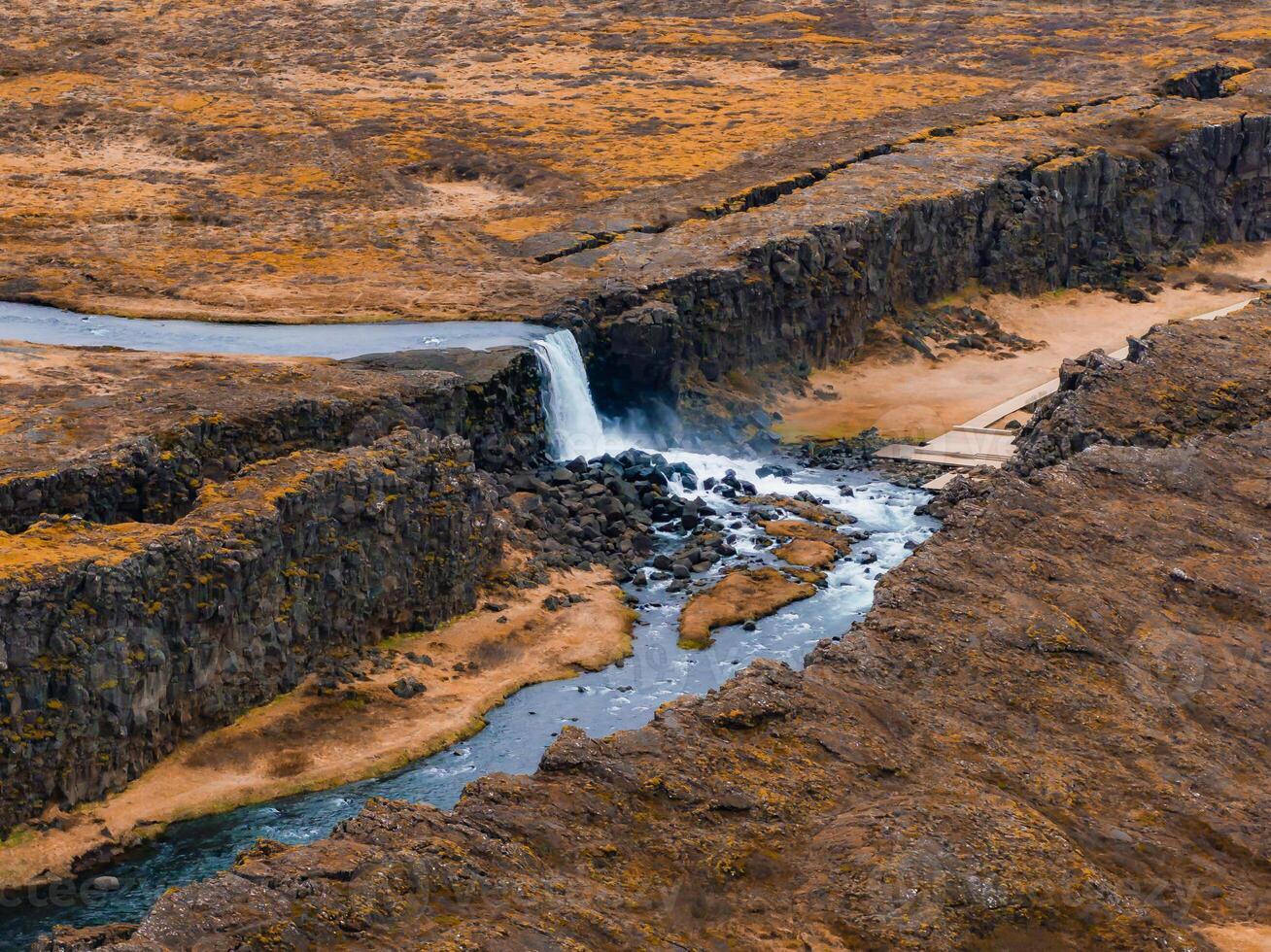 Aerial View of Waterfall Cascading Down Rocky Cliff in Iceland's Volcanic Terrain photo