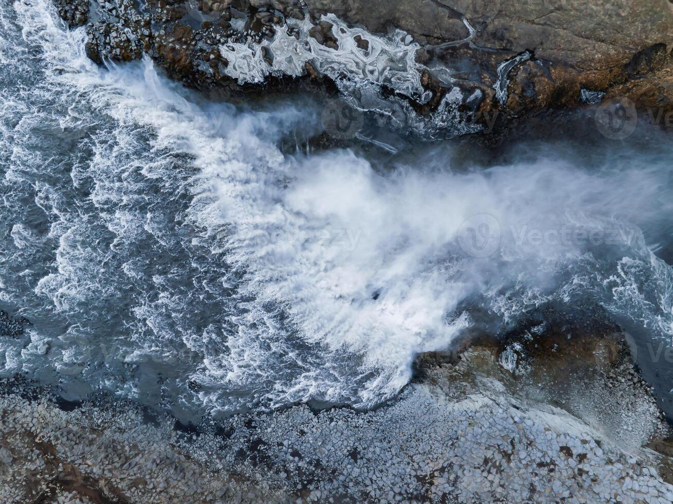 Aerial View of Powerful Waterfall Cascading Over Rugged Rocks in Iceland photo
