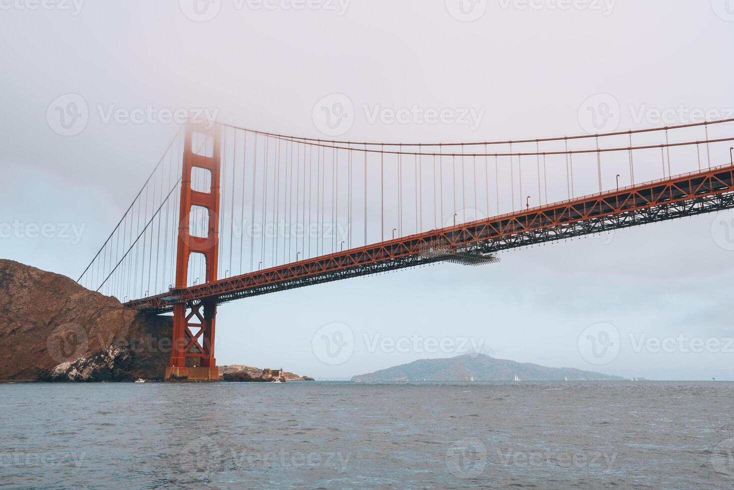 Iconic Golden Gate Bridge in SF, CA. View from water level shows the orange bridge against overcast sky. Tall towers, Marin Headlands visible. Serene scene. photo