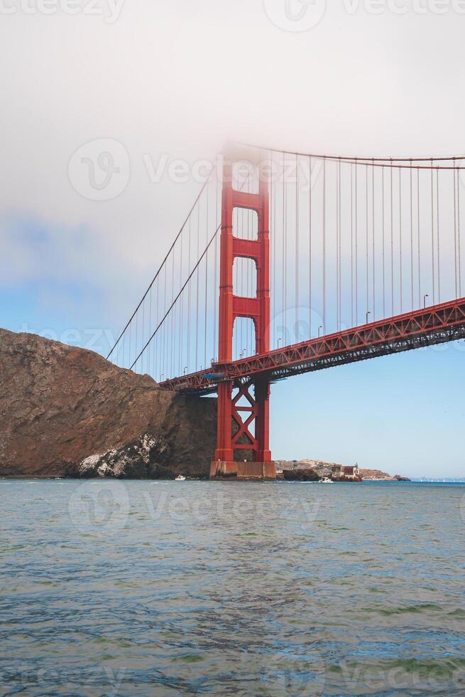 Discover the mesmerizing Golden Gate Bridge in San Francisco, California. Captured from water level, this iconic landmark stands tall with vibrant red orange against a calm blue sky. photo