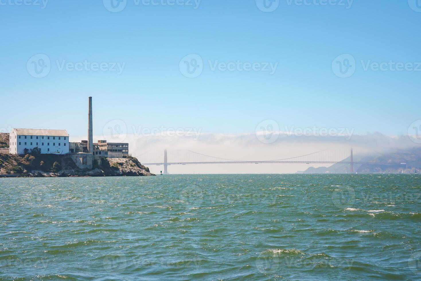 View of Alcatraz Island in San Francisco Bay, CA, USA. The Federal prison buildings and the Golden Gate Bridge are visible in the backdrop, creating a contrast between nature and history. photo
