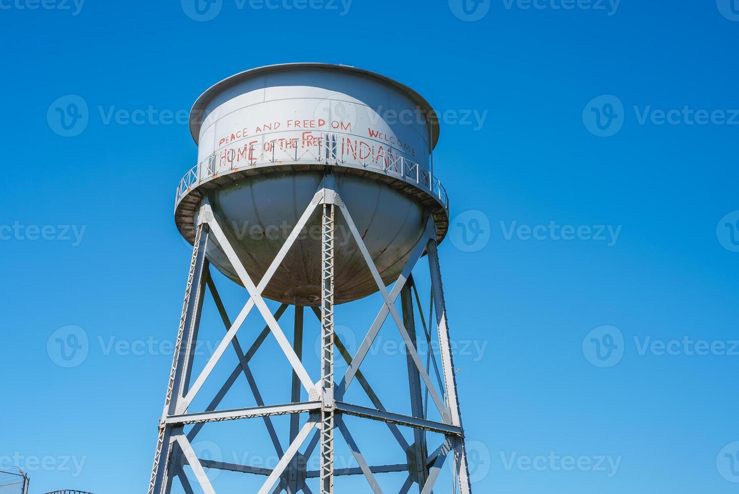 Tall white water tower with conical top, metal lattice beams, PEACE AND FREEDOM WELCOME HOME OF THE FREE INDIAN LAND message. Location Alcatraz Island, San Francisco, USA. photo