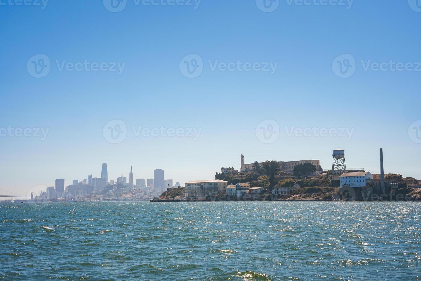 Clear day view of Alcatraz Island from the water, showcasing the infamous prison with cityscape of San Francisco in the background. Serene atmosphere. photo