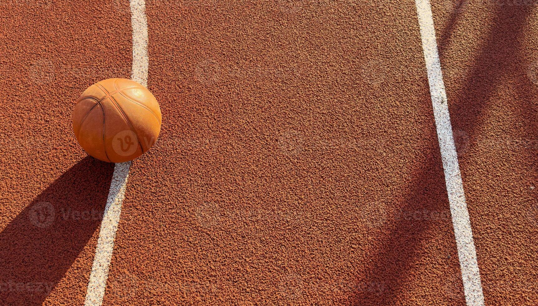 Basketball ball on the ground. Close-up ball on the red court. Basketball on the street or indoor court. Sports gear without people. Minimalism. Template, sport background photo