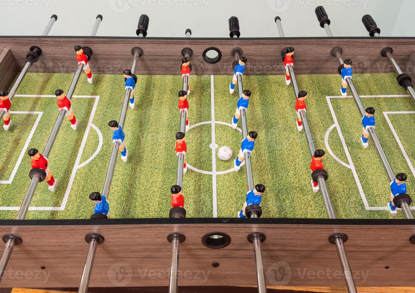 Classic Foosball Table Game With Players in Red and Blue Jerseys During Daytime Indoor Match. Close-up view of foosball table featuring red and blue jersey players positioned for daytime indoor game. photo