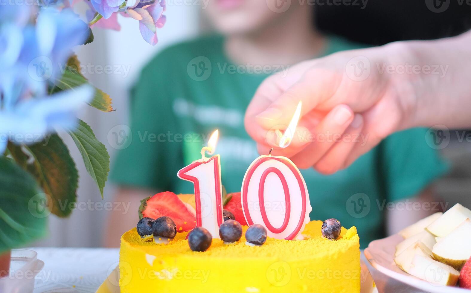 A person lighting a candle on a yellow cake with number 10 photo