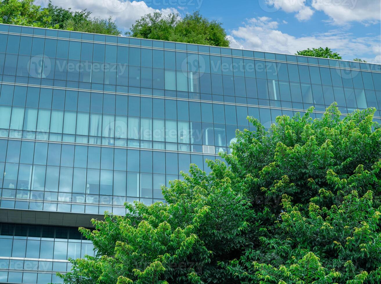 Eco-friendly building in modern city. Sustainable glass office building with trees for reducing carbon dioxide. Office building with green environment. Corporate building reduce CO2. Net zero emission photo