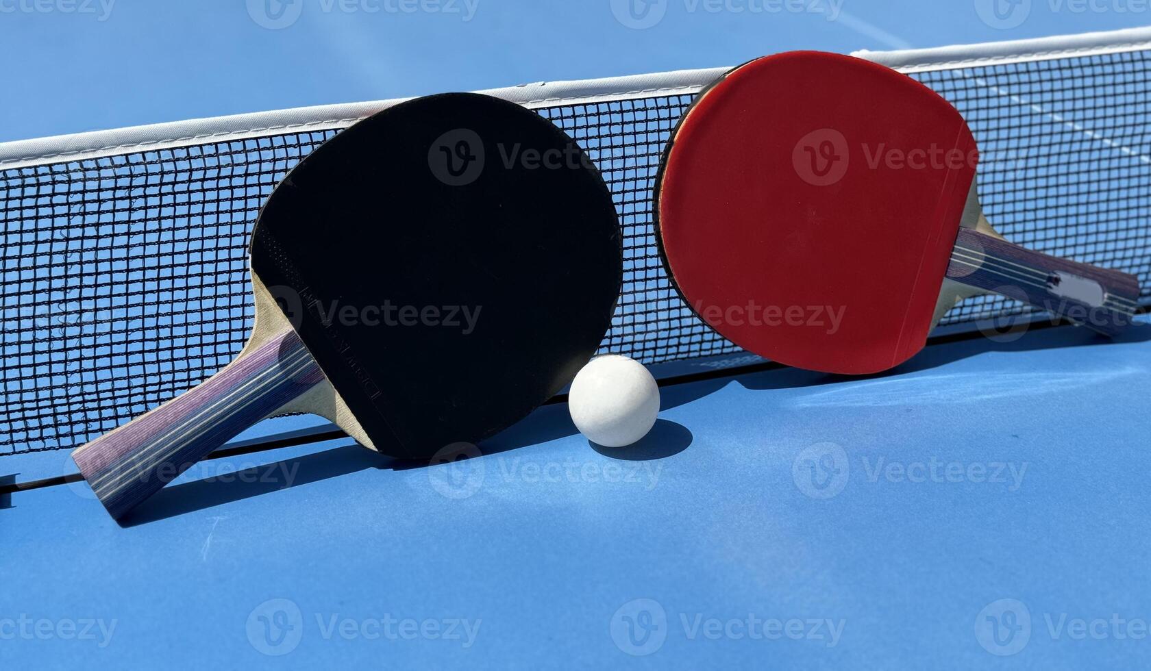 Two table tennis rackets and balls on a blue table with net. photo