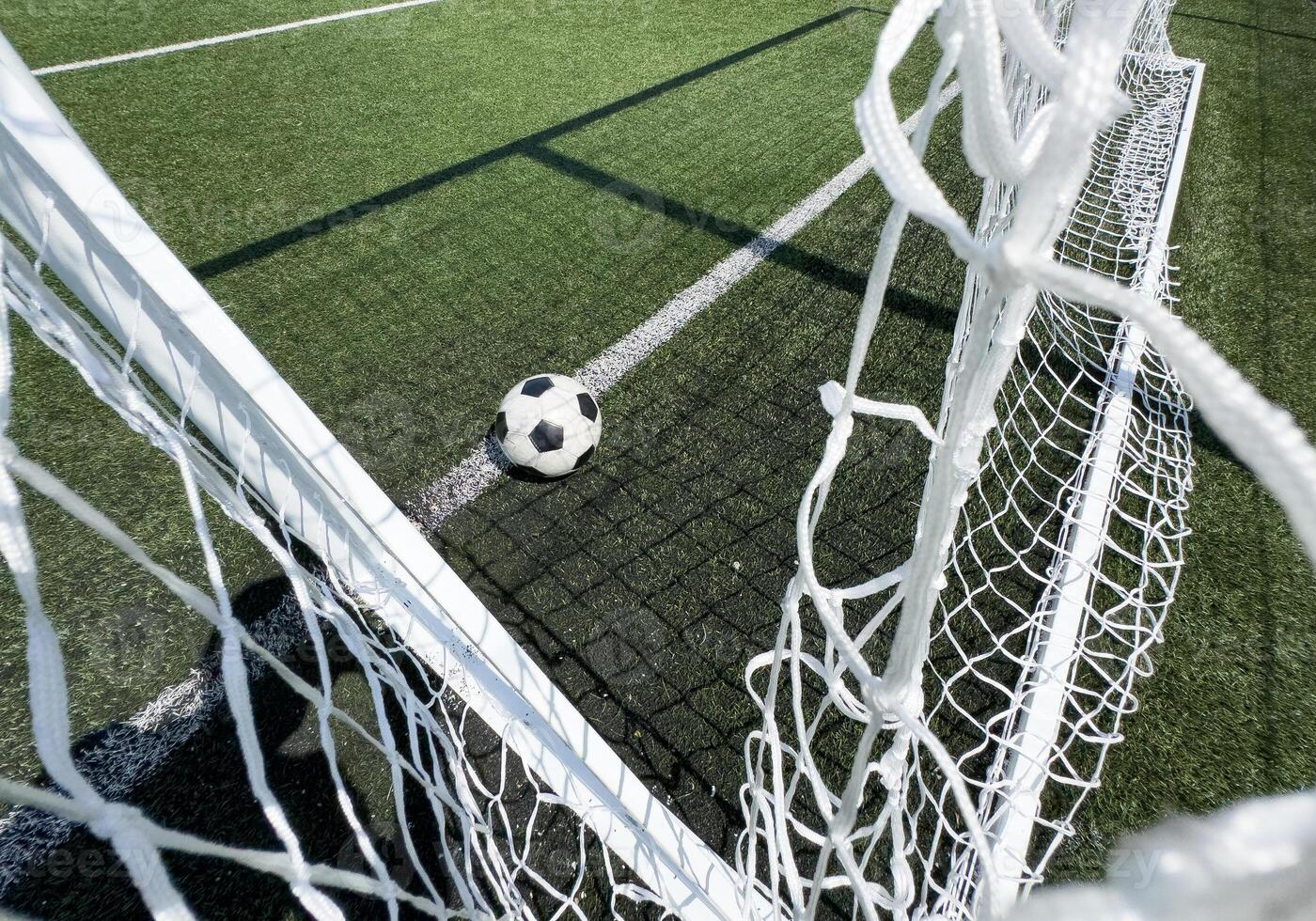Soccer football in Goal net with green grass field. For sport concept. photo