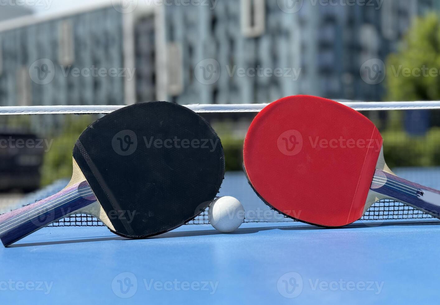 Two table tennis rackets and balls on a blue table with net. photo