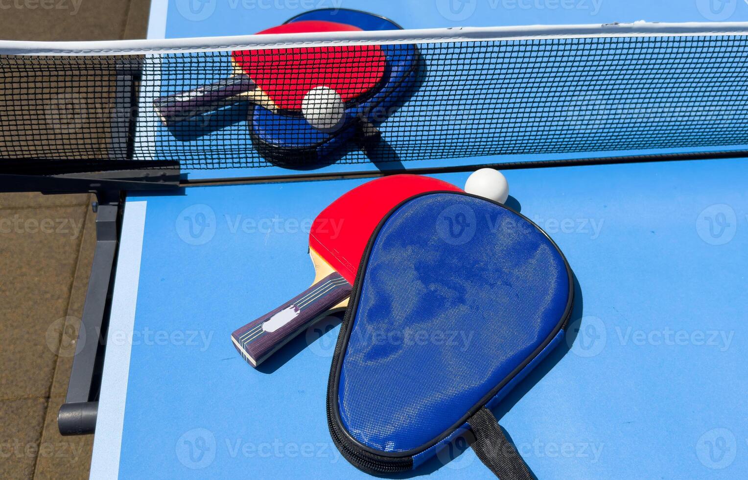Two table tennis rackets and balls on a blue table with net. photo