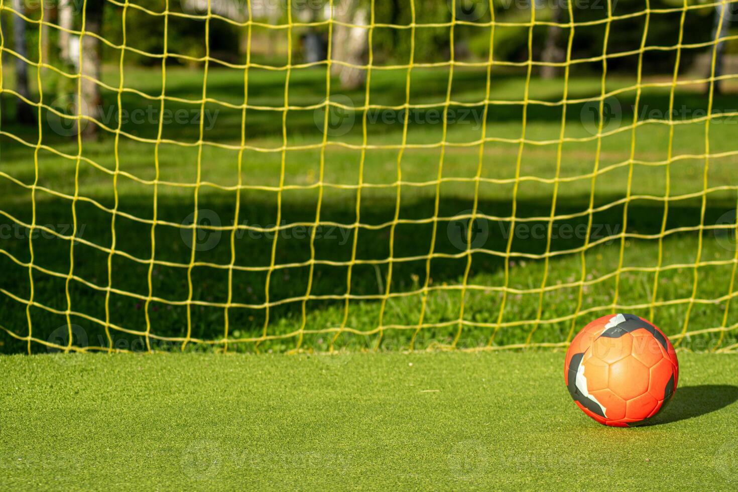 red soccer ball with the yellow net of a goal on an artificial grass football field photo