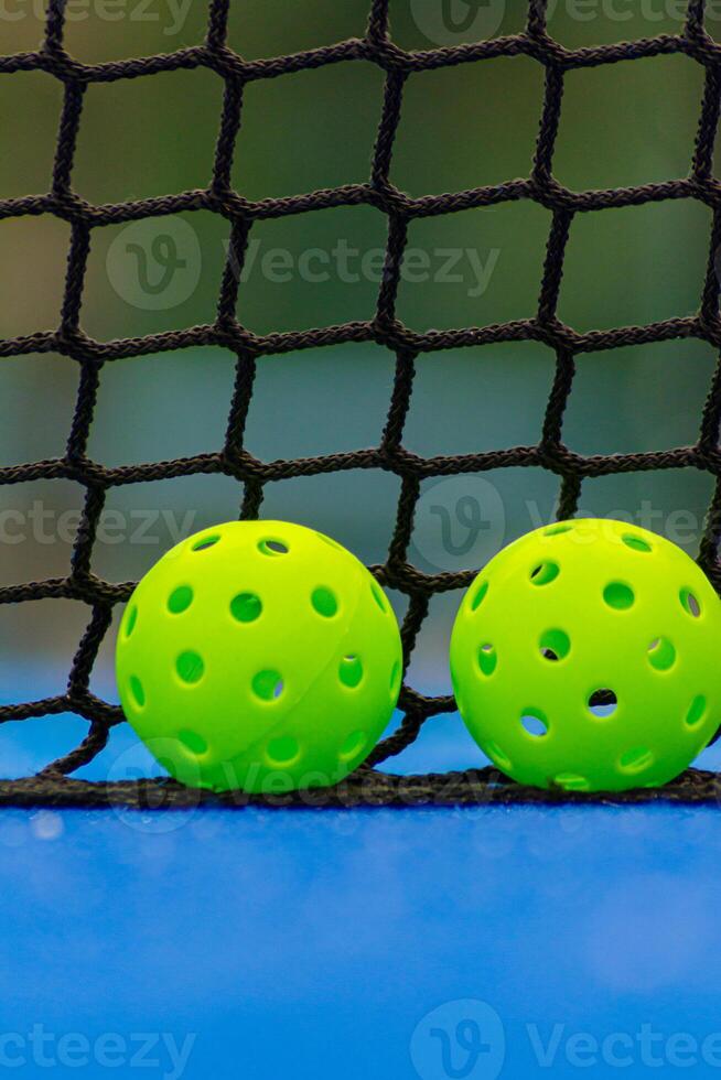two green pickleball balls next to the net of a pickleball court photo