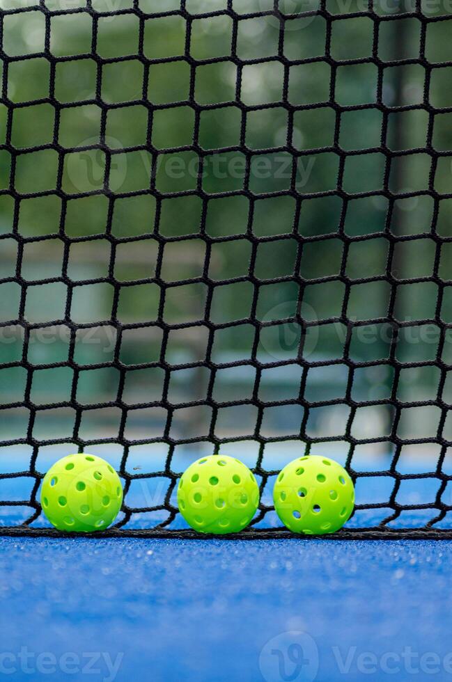 three green pickleball balls next to the net of a pickleball court, new racket sport photo