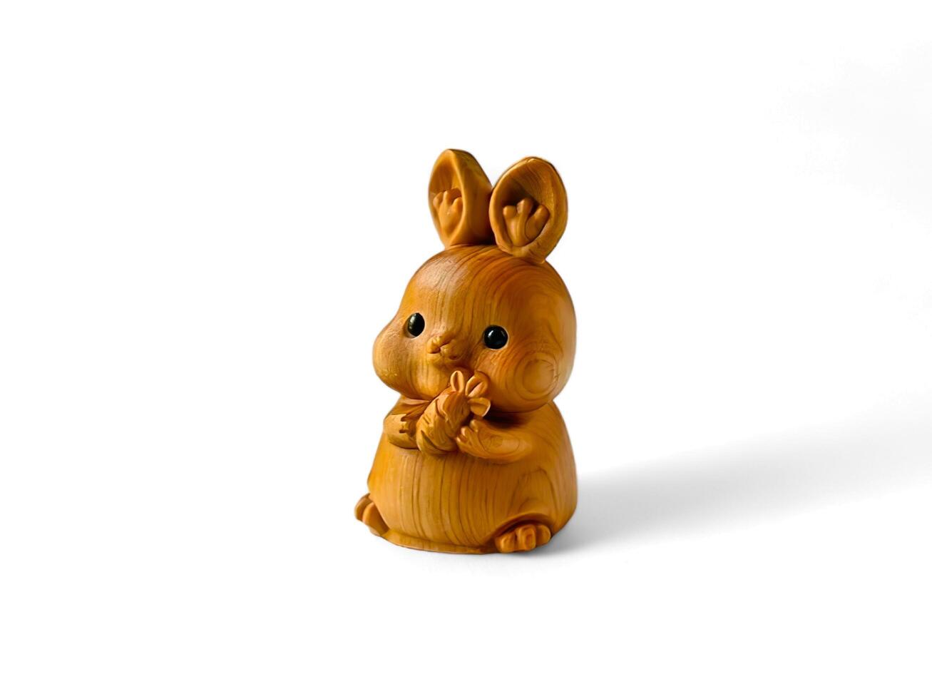 Cute wooden miniature of a rabbit holding a carrot on a white background photo