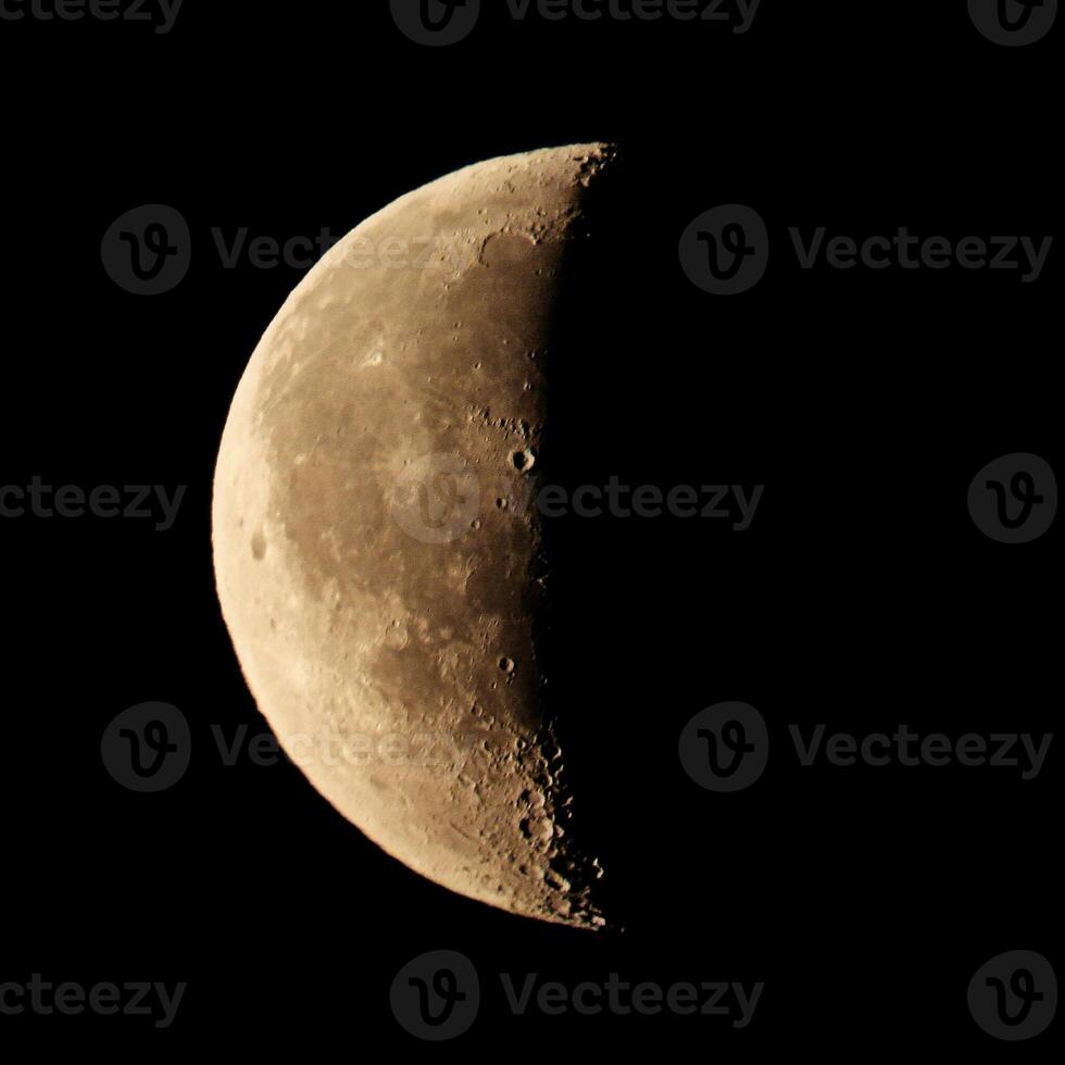 Close up view on a yellow half disk of the moon on a black sky background photo